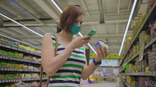 30名妇女面对保护面罩在手机的帮助下在罐子上阅读杂货视频