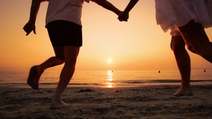 在海滩上奔跑的情侣在海边日落手牵手和缓慢地跳跃男人30秒视频