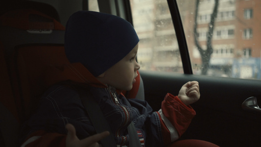 男孩坐在儿童座位上的汽车中骑着男孩在雨季看着窗外视频