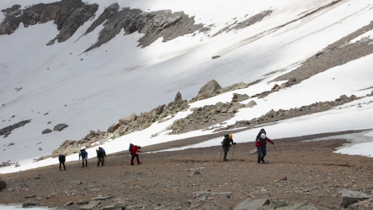 一群疲倦的徒步者正在山上用徒步杆和头盔在斜坡上登山视频