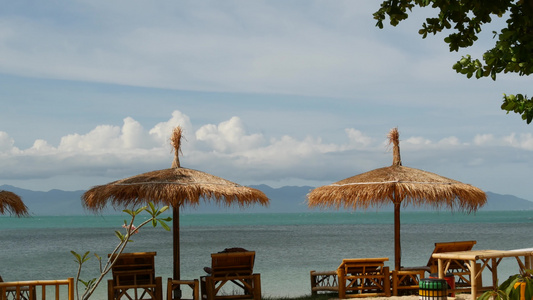 海背景上的遮阳伞从稻草和棕榈树的太阳伞在海洋和天空视频