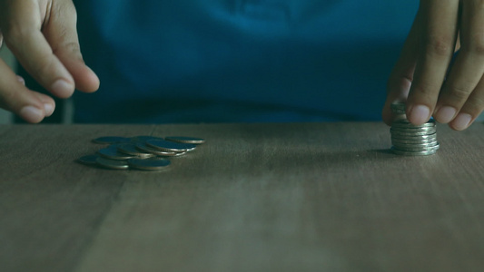 身穿蓝衬衫的女人在棕色木制桌子上堆积硬币视频