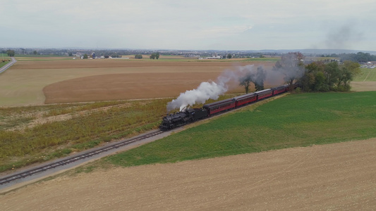 从角度看一个已恢复的蒸汽机在拖着古型客车驶往农田时发视频