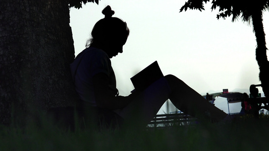 在公园树旁读书的年轻有吸引力的青年女子双影女郎视频