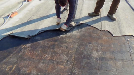 工人将受损的沥青层从建筑物平板屋顶上移走视频