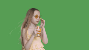 十几岁的女孩用吸管从透明绿色背景的玻璃上喝橙汁年轻21秒视频