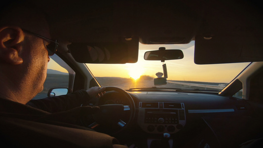 男子驾驶汽车沿高速公路日落的阳光照耀着挡风玻璃视频