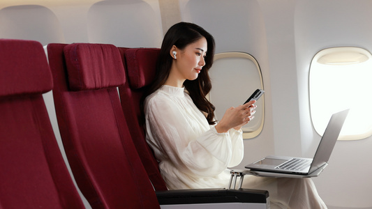 年轻美女坐在机舱座椅上浏览手机页面视频