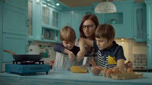 母亲和两个儿子在家里的蓝色厨房里一起煮炒鸡蛋的幸福家庭16秒视频