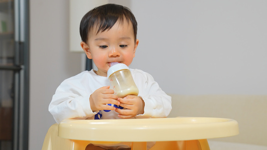 男宝宝坐在餐椅上抱着奶瓶喝奶视频