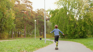 在美丽的绿公园里骑滑板的可爱少年男孩21秒视频