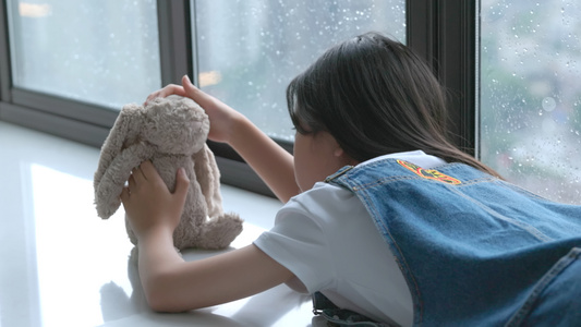 小女孩趴在窗台上抚摸小熊玩偶视频