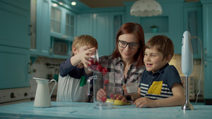 幸福的母亲和两个孩子在家里的蓝色厨房里用搅拌机做果酱35秒视频