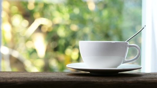 木制桌上的白陶瓷咖啡杯和树底模糊的杯子上的蒸汽视频