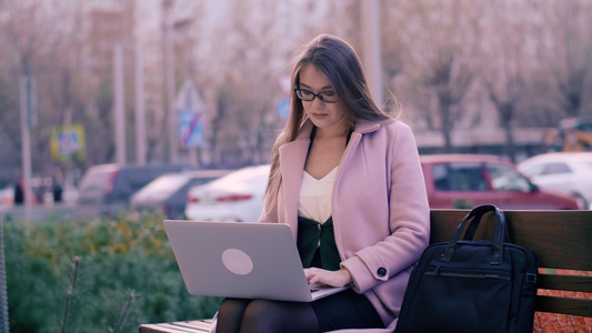 坐在长椅上和在城市公园背景中使用笔记本电脑的妇女视频