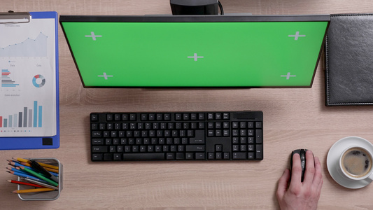 一名在电脑上工作的男子的顶部视图显示器上有绿色屏幕视频