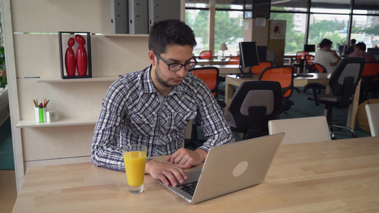 英俊的男人用笔记本电脑工作喝橙汁视频