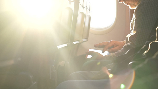 通过飞机窗口日落男人在国际飞行中使用平板电脑的人视频