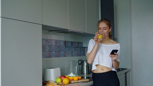 美丽的女孩喝杯子上新鲜橙汁女人用智能手机11秒视频