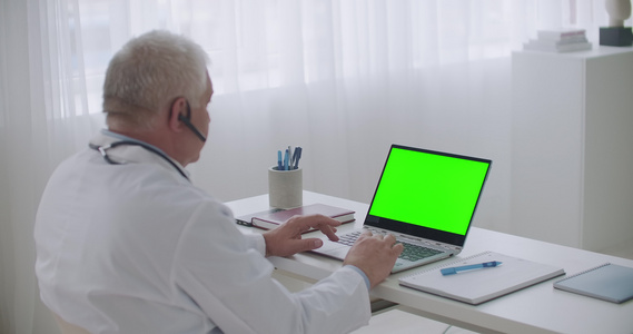 男性医生正在用笔记本电脑观看和收听网络研讨会绿色显示视频