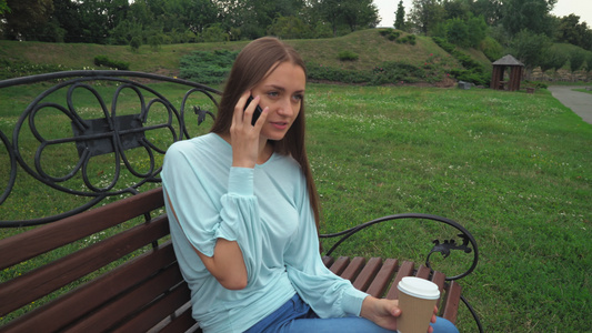 一名年轻女孩坐在公园长椅上通过电话交谈视频