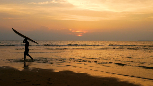 4K年轻快乐冲浪男子在日落时分在热带海滩上用长冲浪板视频