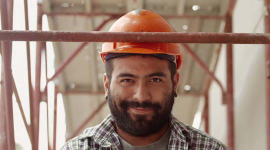 年轻的拉丁男子在建筑工地工作微笑着看着相机视频
