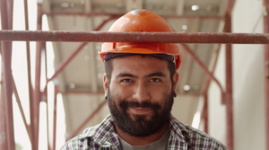年轻的拉丁男子在建筑工地工作微笑着看着相机12秒视频