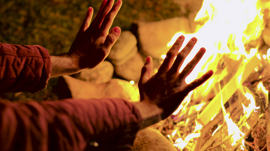 在秋天寒冷的夜晚青年男子在营火中将他的手暖和起来视频