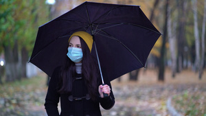 一位戴着防护面具的年轻女子在雨伞下在公园里散步下雨天11秒视频