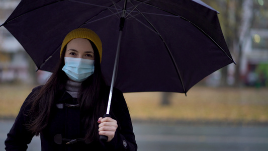 一位戴着防护面具的年轻女子在雨伞下在公园里散步视频