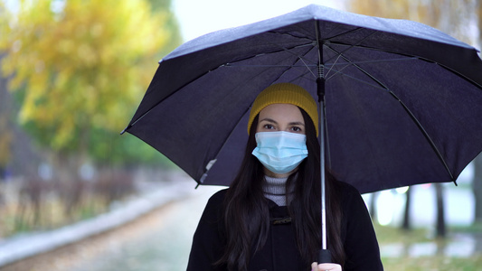 一位戴着防护面具的年轻女子在雨伞下在公园里散步下雨天视频