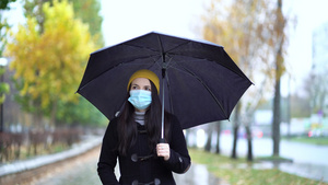 一位戴着防护面具的年轻女子在雨伞下在公园里散步15秒视频