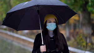 一位戴着防护面具的年轻女子在雨伞下在公园里散步下雨天21秒视频