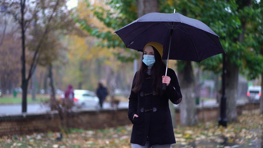 一位戴着防护面具的年轻女子在雨伞下在公园里散步下雨天视频