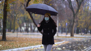 一位戴着防护面具的年轻女子在雨伞下在公园里散步下雨天10秒视频