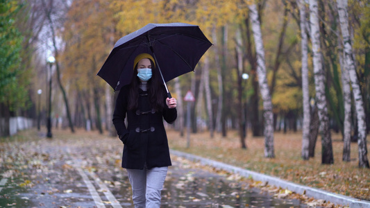 一位戴着防护面具的年轻女子在雨伞下在公园里散步下雨天视频