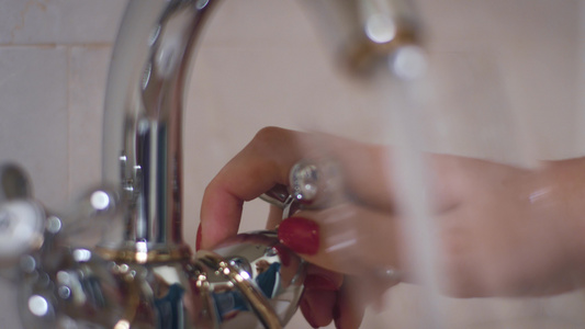 女用手把从水龙头上转把水倒进浴室的玻璃杯视频