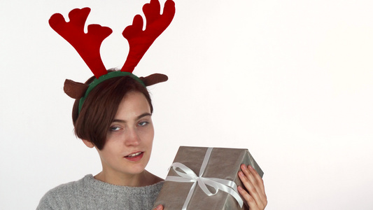穿着驯鹿鹿鹿角的快乐女人头带看着她的圣诞节礼物视频