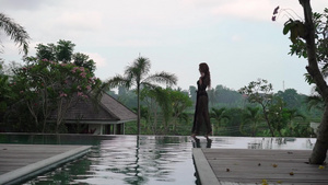 穿黑裙子的年轻性感女人在豪华别墅游泳池附近走11秒视频