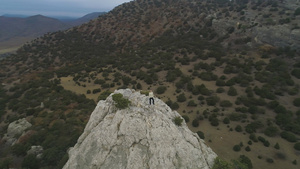 年轻女子正站在离海岸线近的岩石山顶上空中观察无人驾驶20秒视频