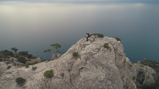 年轻女子站在岩石悬崖顶上背包和徒步杆靠近海岸线空中视频
