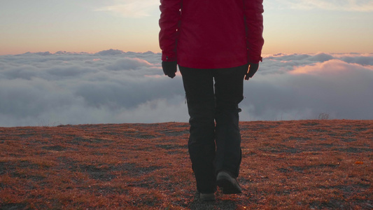 身穿夹克和裤子的年轻女子正步行到云端高山边缘在色彩视频