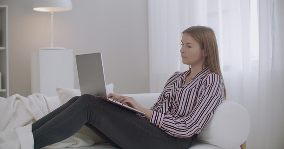 年轻妇女正在浏览互联网使用笔记本电脑坐在家中沙发上视频
