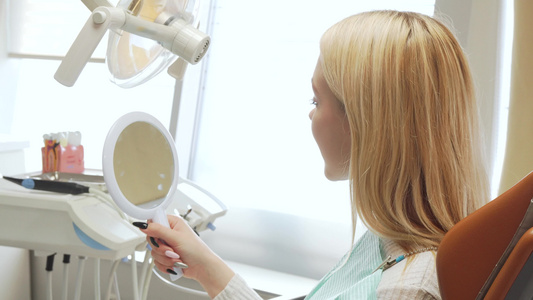 一名女病人在牙科诊所照镜子后仰视镜的后视镜头视频