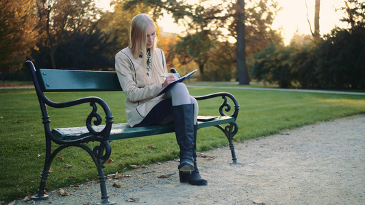 美丽的年轻女子正在公园户外写日记在公园里写日记视频