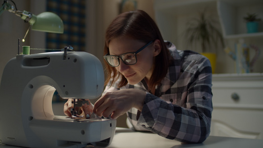 30多岁的年轻女子在家工作的缝纫机上穿针戴眼镜的女视频