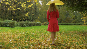 雨天身穿红色裙子打着黄色雨伞的苗条年轻女子在公园12秒视频