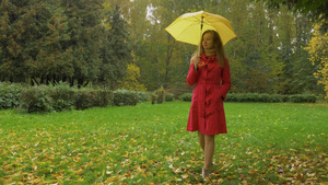 下雨天身穿红色斗篷打着黄色雨伞的苗条年轻女子正走在21秒视频