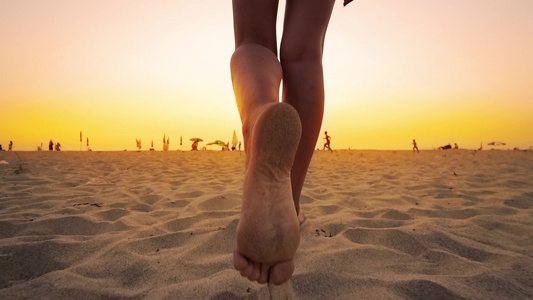 穿着比基尼的年轻女子在日落时在沙沙滩上行走慢动作视频